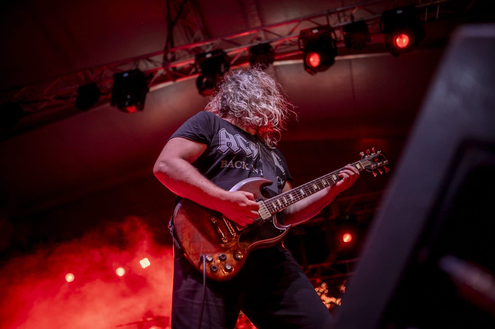 A guitarist playing a Gibson SG under red stage lights at a concert.