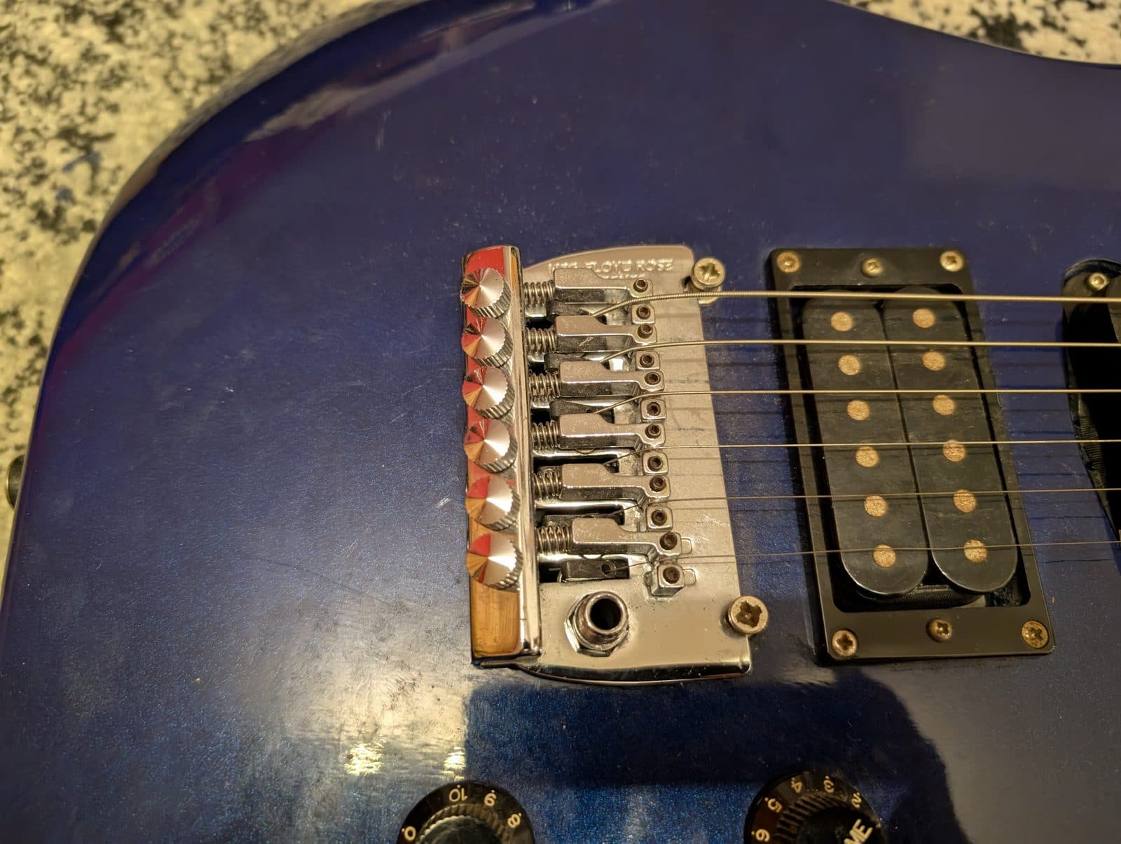 Close-up of a locking tremolo bridge and pickup on a blue electric guitar.