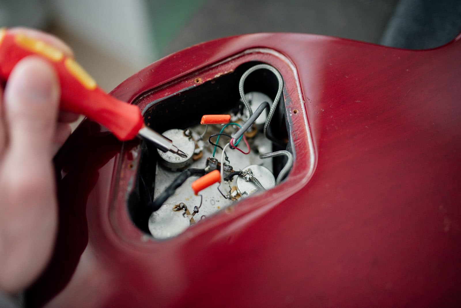 A hand using a screwdriver inside an electric guitar's control cavity during a repair.