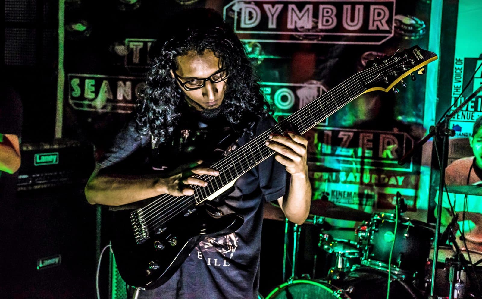 A guitarist playing an eight-string Schecter guitar live on stage.