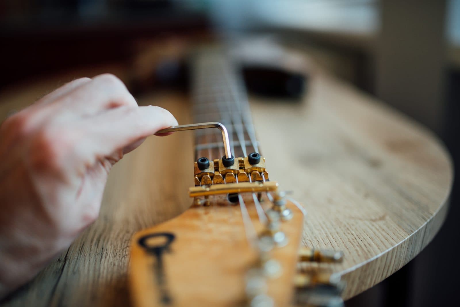 A hand adjusting an electric guitar's bridge saddles with a hex key.