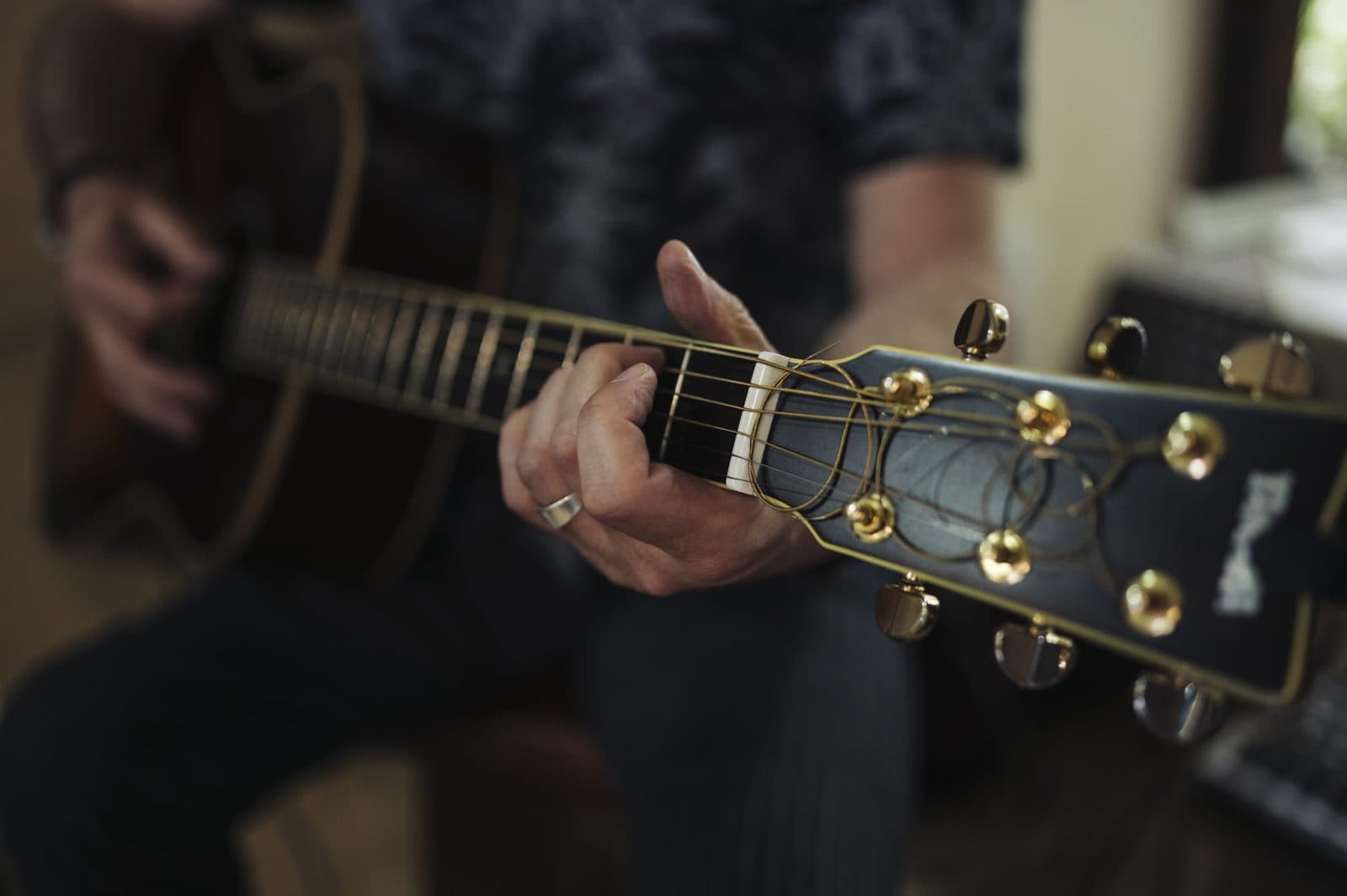 A player's fretting hand pressing strings against the fretboard of an acoustic guitar.