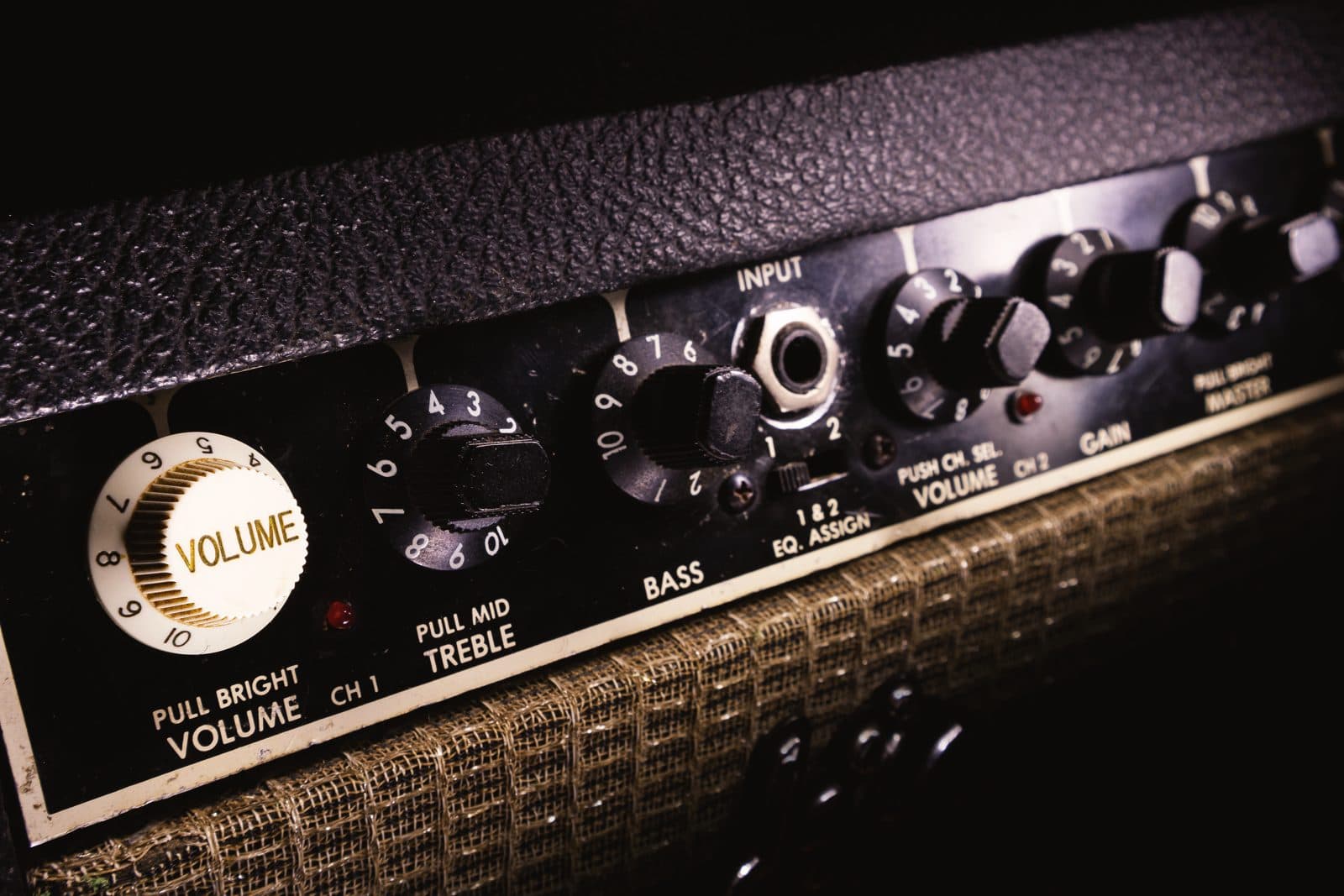 Close-up of a vintage guitar amplifier control panel with volume, treble, bass, and gain knobs.