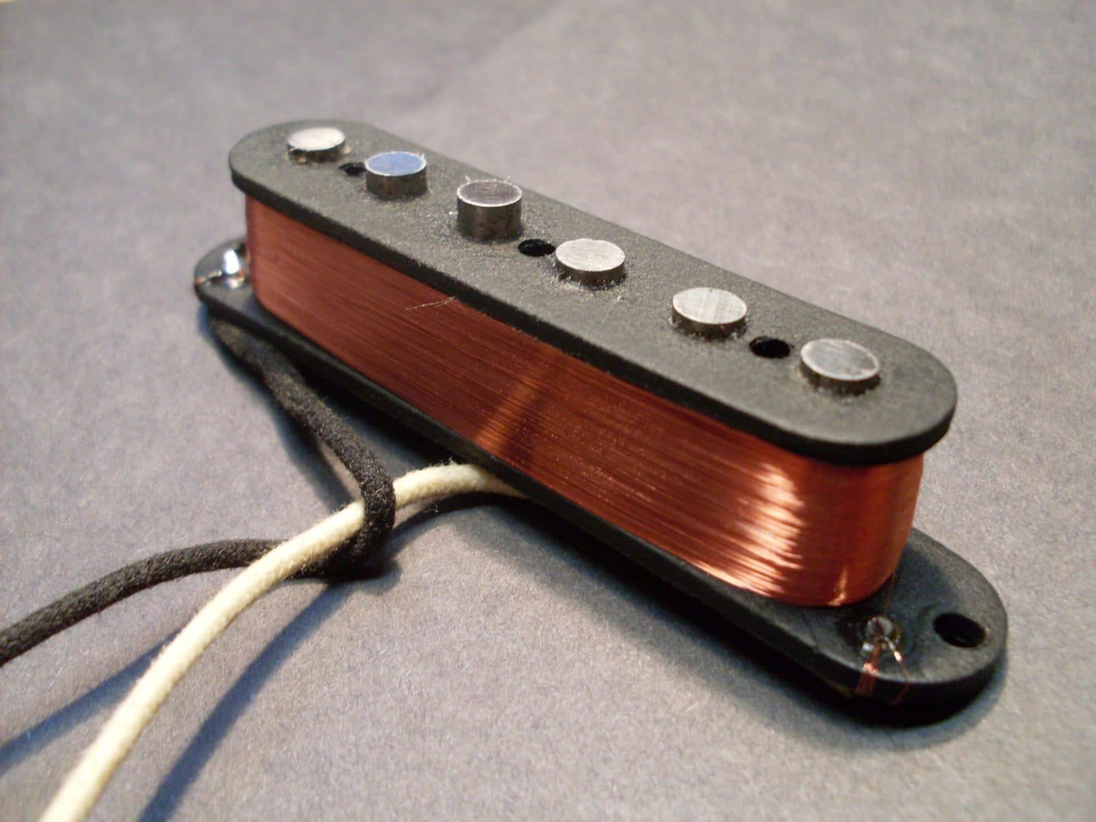 A single-coil guitar pickup with its copper wire winding exposed.