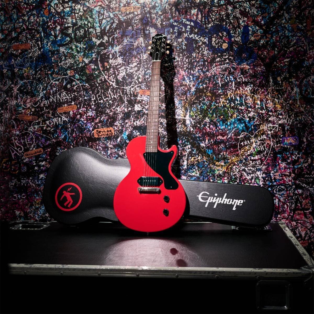 The Epiphone Billie Joe Armstrong Les Paul Junior in Radiant Red, leaning against its black hardshell case backstage