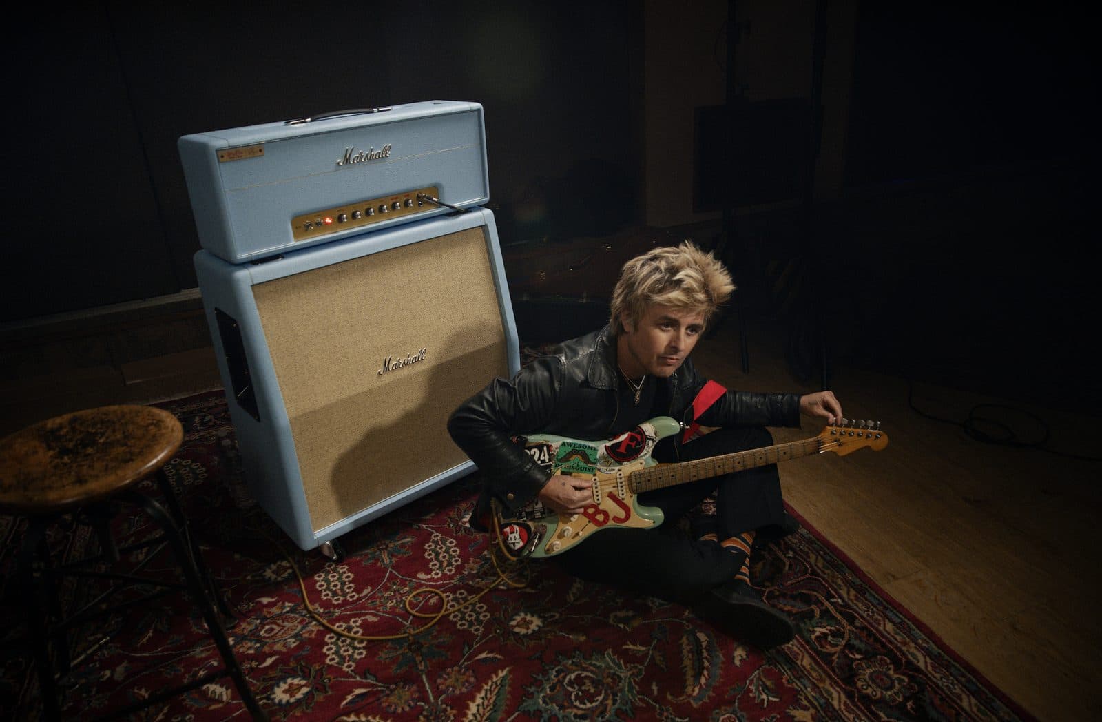 The baby-blue Marshall 1959BJA Billie Joe Armstrong signature amp head and cabinet, with Armstrong seated beside it holding his Fender Blue